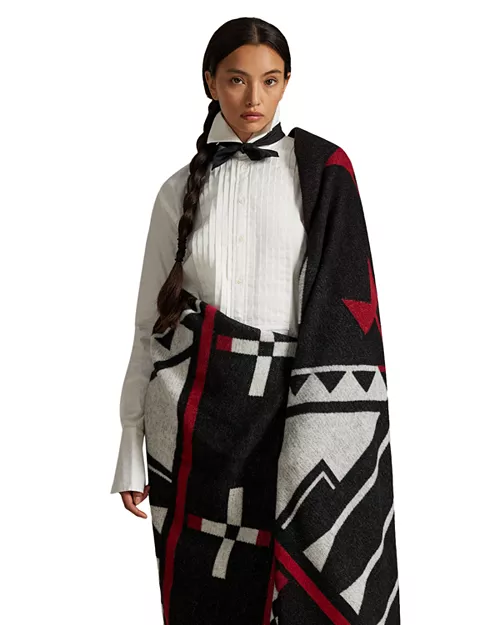A model showcases a stylish blanket featuring Native American-inspired patterns, wrapped elegantly around her shoulders while wearing a classic white shirt and bowtie.