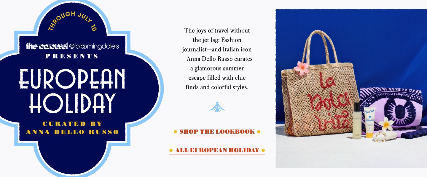 1 photo, a large woven tote bag with La Dolce Vita written in script on the side, a rolled up purple beach towel with an eye illustration, 2 skincare bottles, and a bracelet on a white counter with a dark blue background.