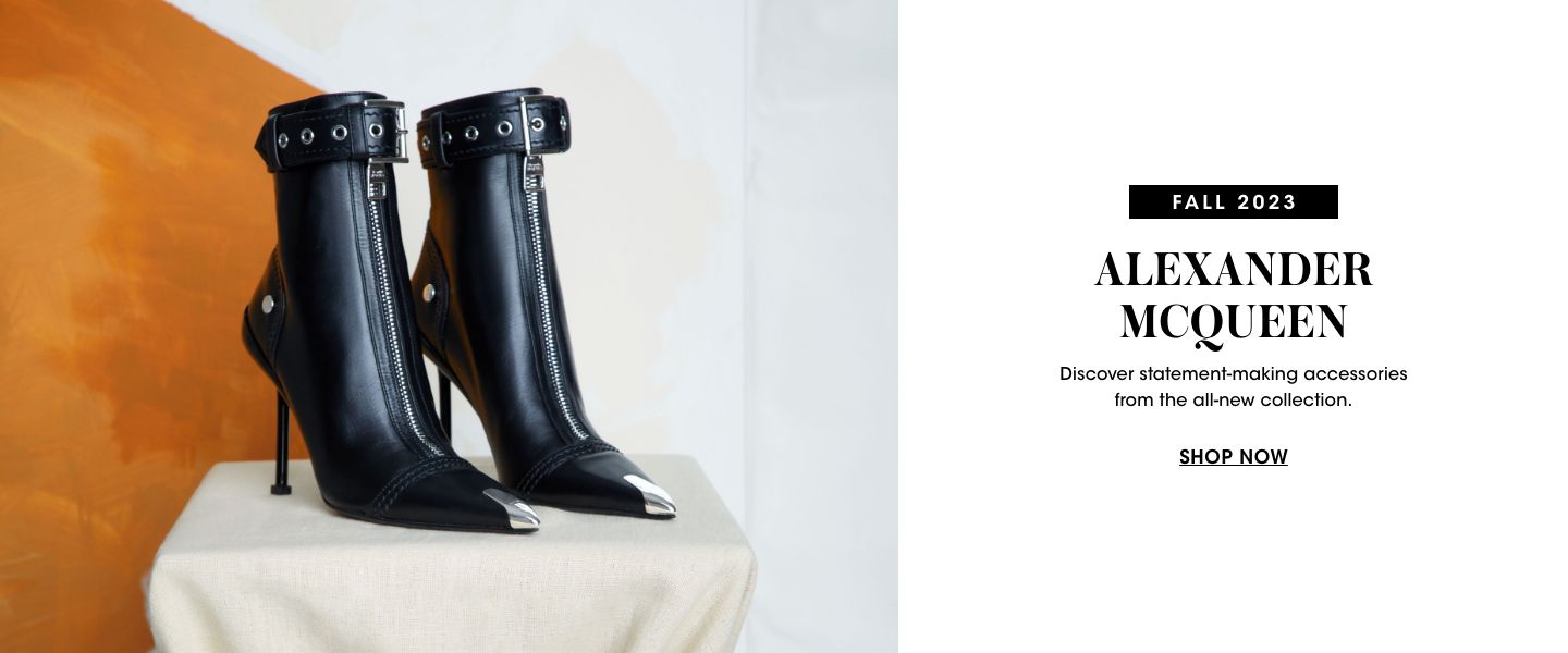 1 photo, of a pair of black Alexander McQueen high heel boots with silver topped toes and buckles at the top, sitting atop a cloth wrapped pedestal in front of a tan and white wall.