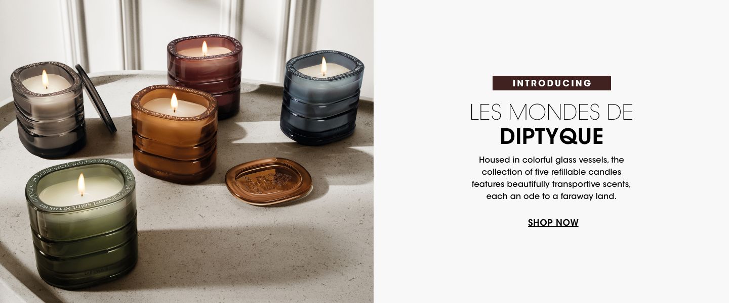 1 photo, of the five lit Diptyque candles in glass jars of dark blue, amber, silver, green, and maroon, on a white countertop.