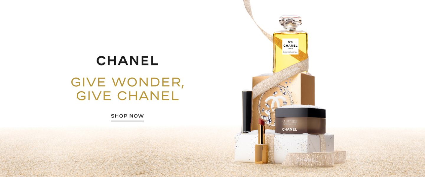 1 photo, of a bottle of Chanel number 5 on top of a gold box with the Chanel logo, and a chanel lipstick and bottle of skincare on a white package with a gold ribbon that winds around the perfume bottle.