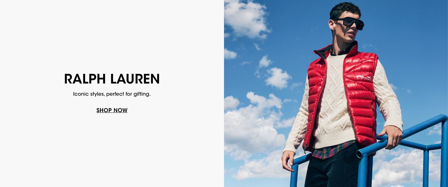1 photo, of male model standing outside with blue skies behind him, wearing a Ralph Lauren red puffer vest, white cable knit sweater, blue pants, and sunglasses.
