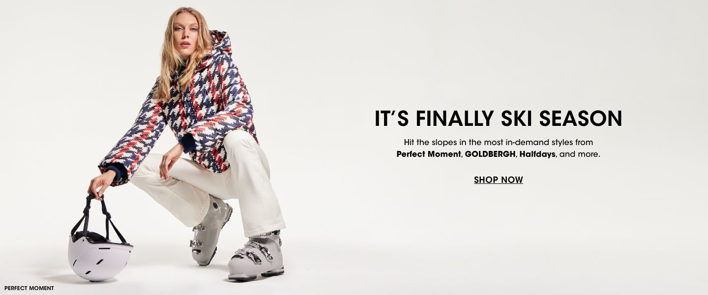 1 photo, of a female model in a red, white, and blue squiggly striped Perfect Moment ski coat and white ski pants, holding a ski helmet.