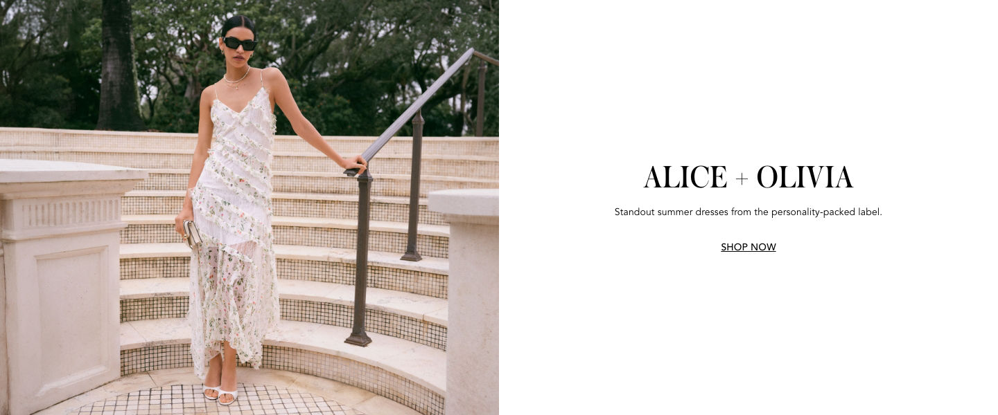 1 photo, of a female model standing at the bottom of curved marble steps, one arm holding a railing, wearing an Alice and Olivia white flowery, lacy maxi dress and sunglasses.