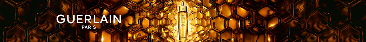 A golden bottle of Guerlain Abeille Royale serum surrounded by a golden honeycomb set.