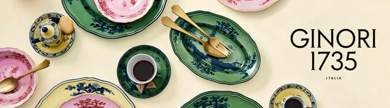 1 photo, an ariel shot of Ginori 1735 dinnerware in green, pink, and yellow, a gold color fork and spoon on an oval platter, a filled tea mug on a tea saucer.