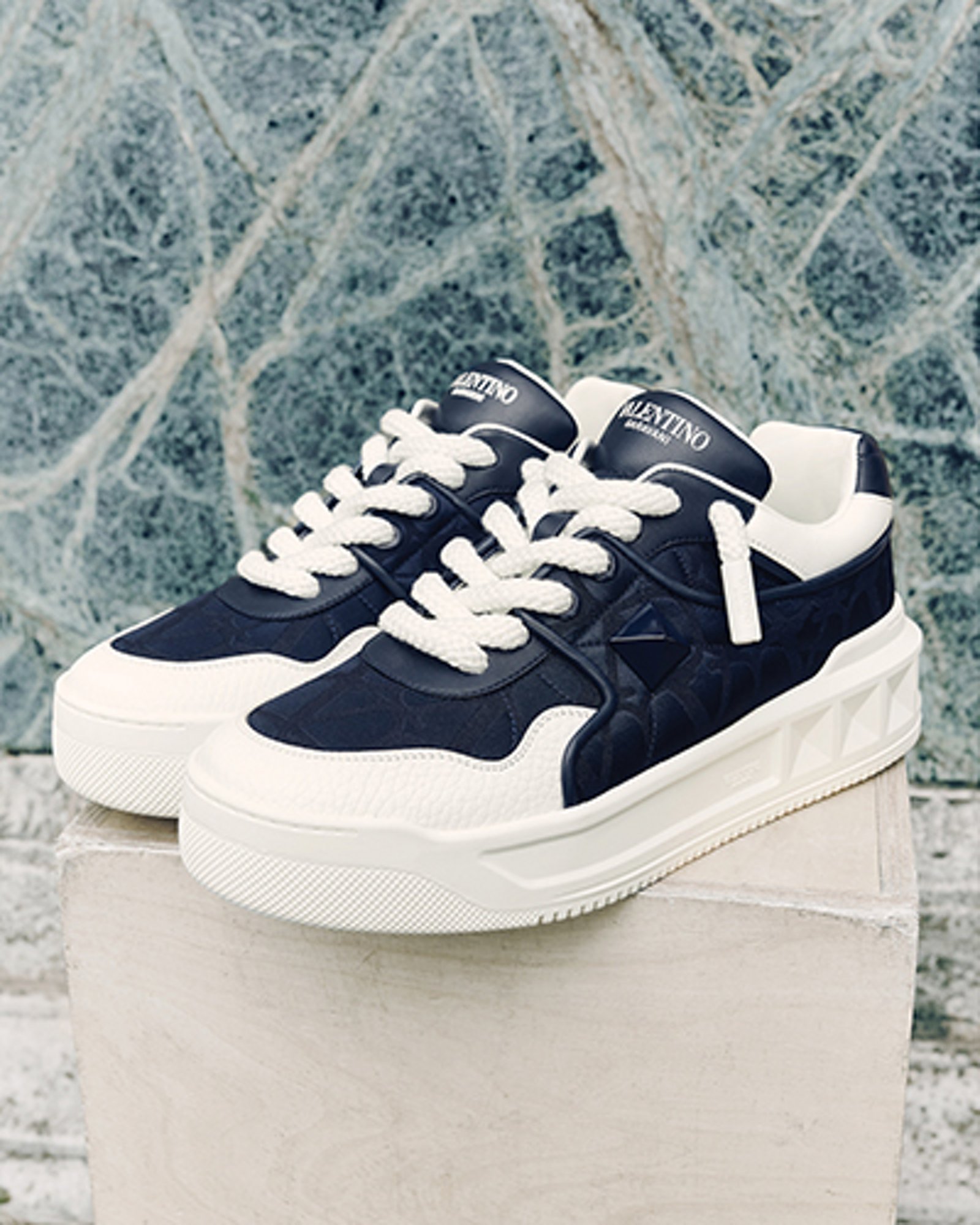 1 photo of mens Valentino black and white sneakers set on a marble pedestal.