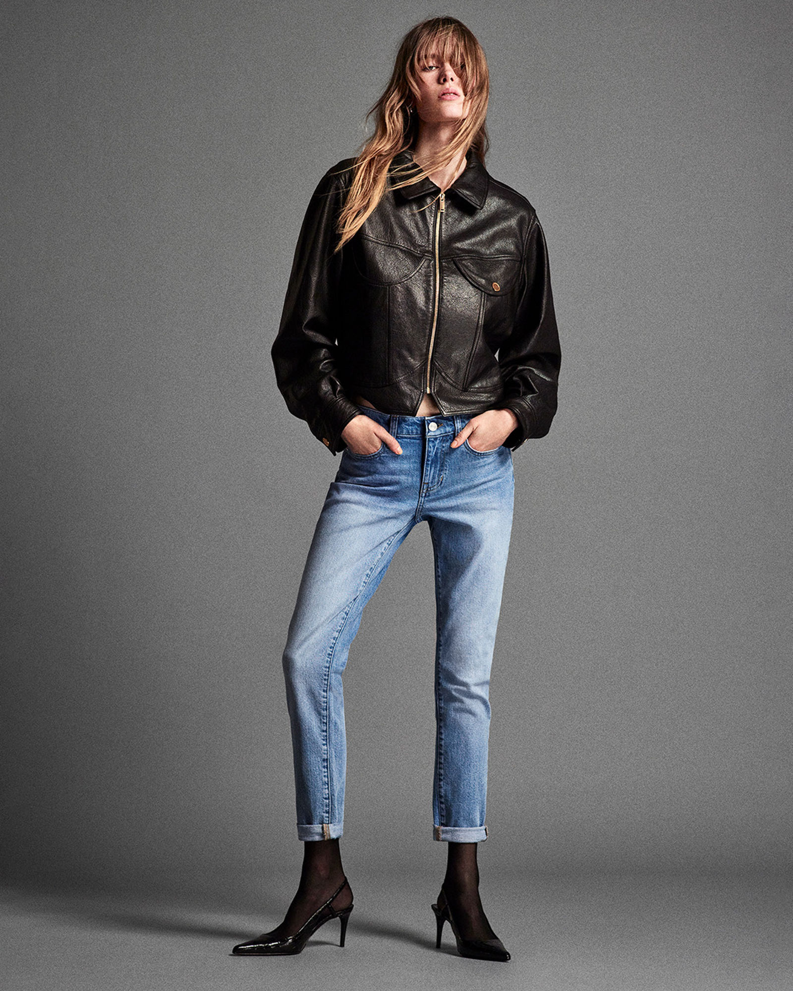 1 photo of female model in black Frame leather jacket, fitted light wash denim jeans, and black heels.