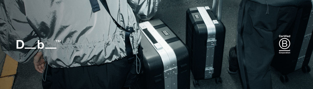 1 photo, of the backs of 2 people in black pants and silver jackets walking with black and silver hard case D. B. roller luggage bags.