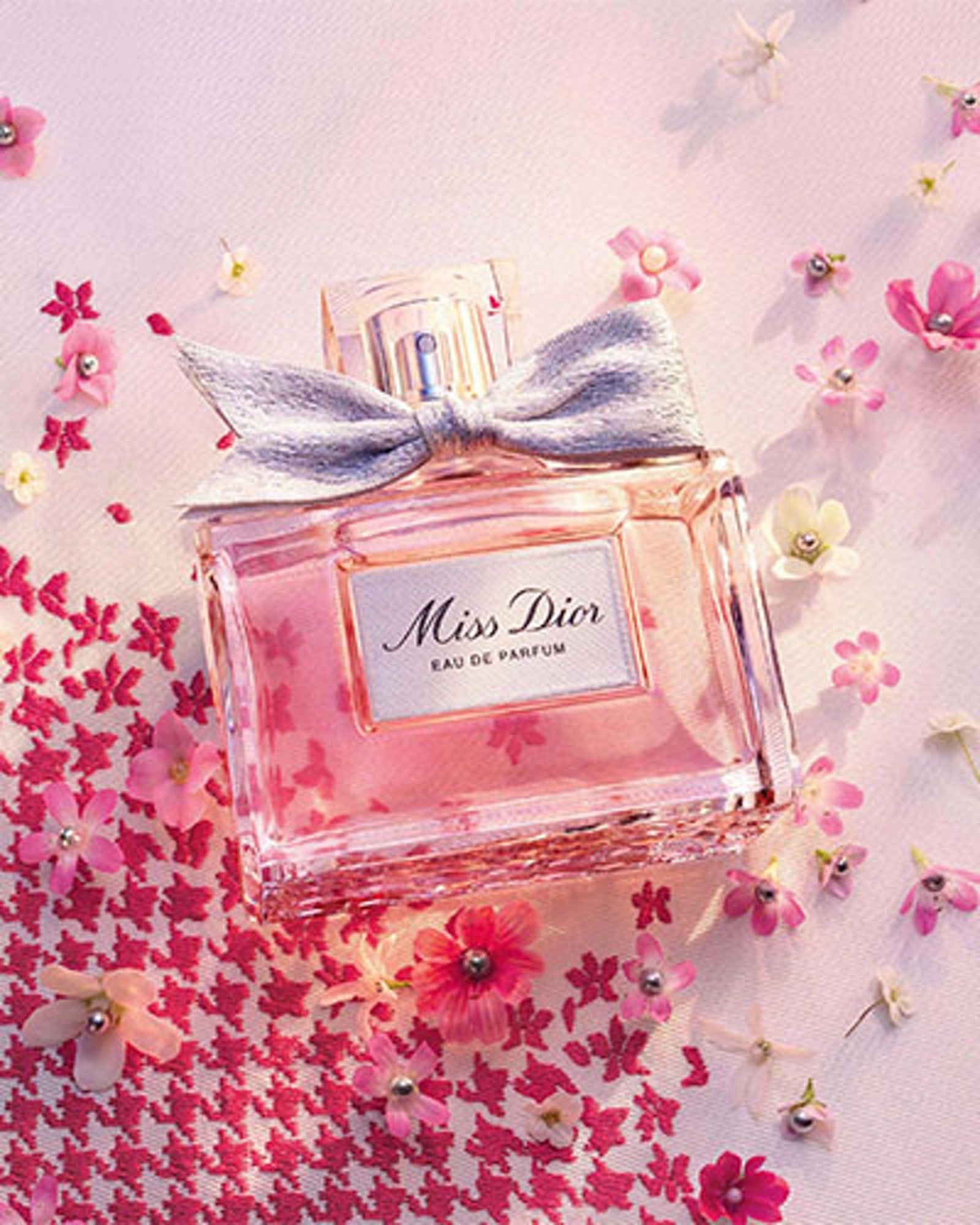 1 photo of Miss Dior fragrance bottle resting on a table with crafting flowers scattered around it.