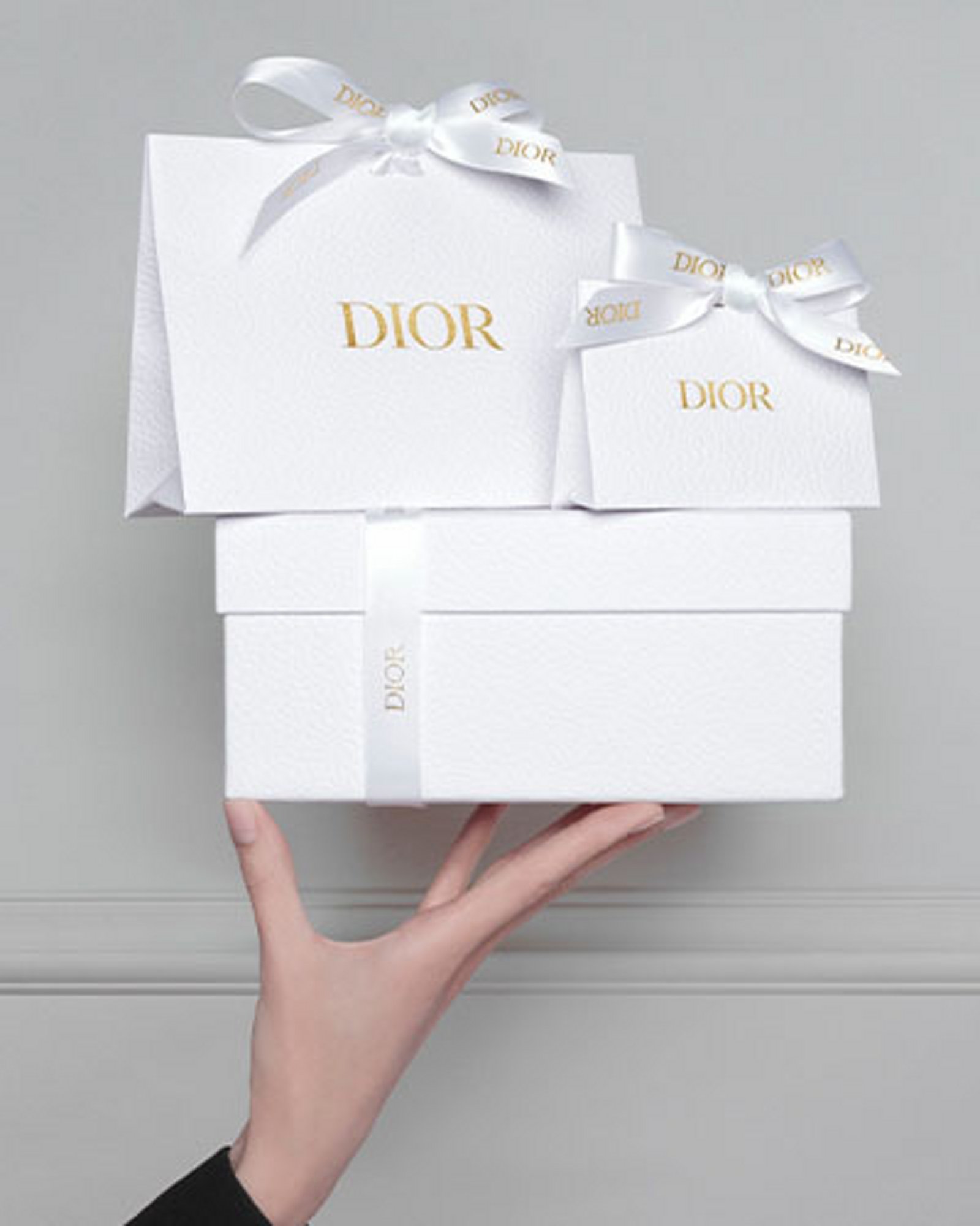 1 photo of 1 white gift box and 2 white gift bags with the Dior log and each item decorated with white ribbons with the Dior logo.