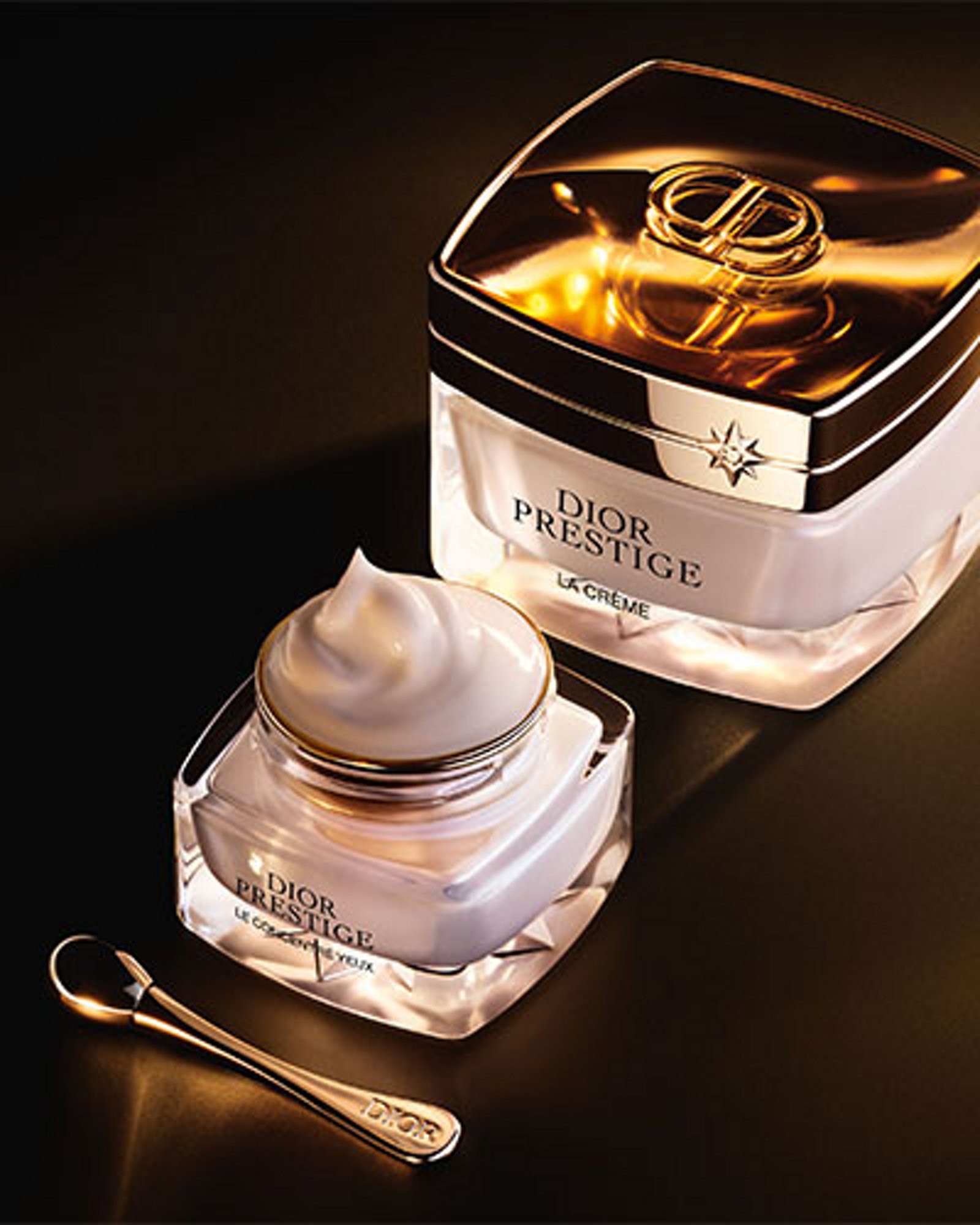 1 photo of Dior Prestige bottles, 1st smaller bottle opened with cosmetic spoon in front of 2nd larger bottle, that's closed with lid.