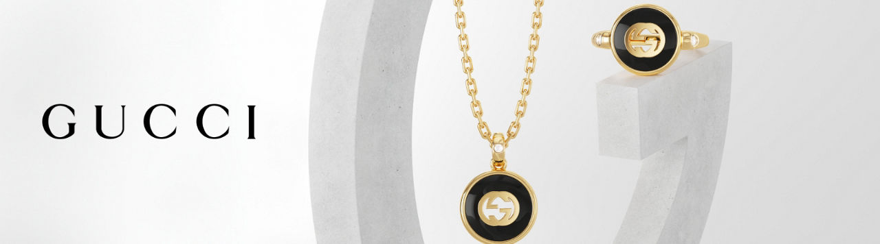 1 photo, of a Gucci round pendant in black and yellow gold with the Gucci logo in the center hanging on a yellow gold link chain from a marble G, a matching ring across from it.