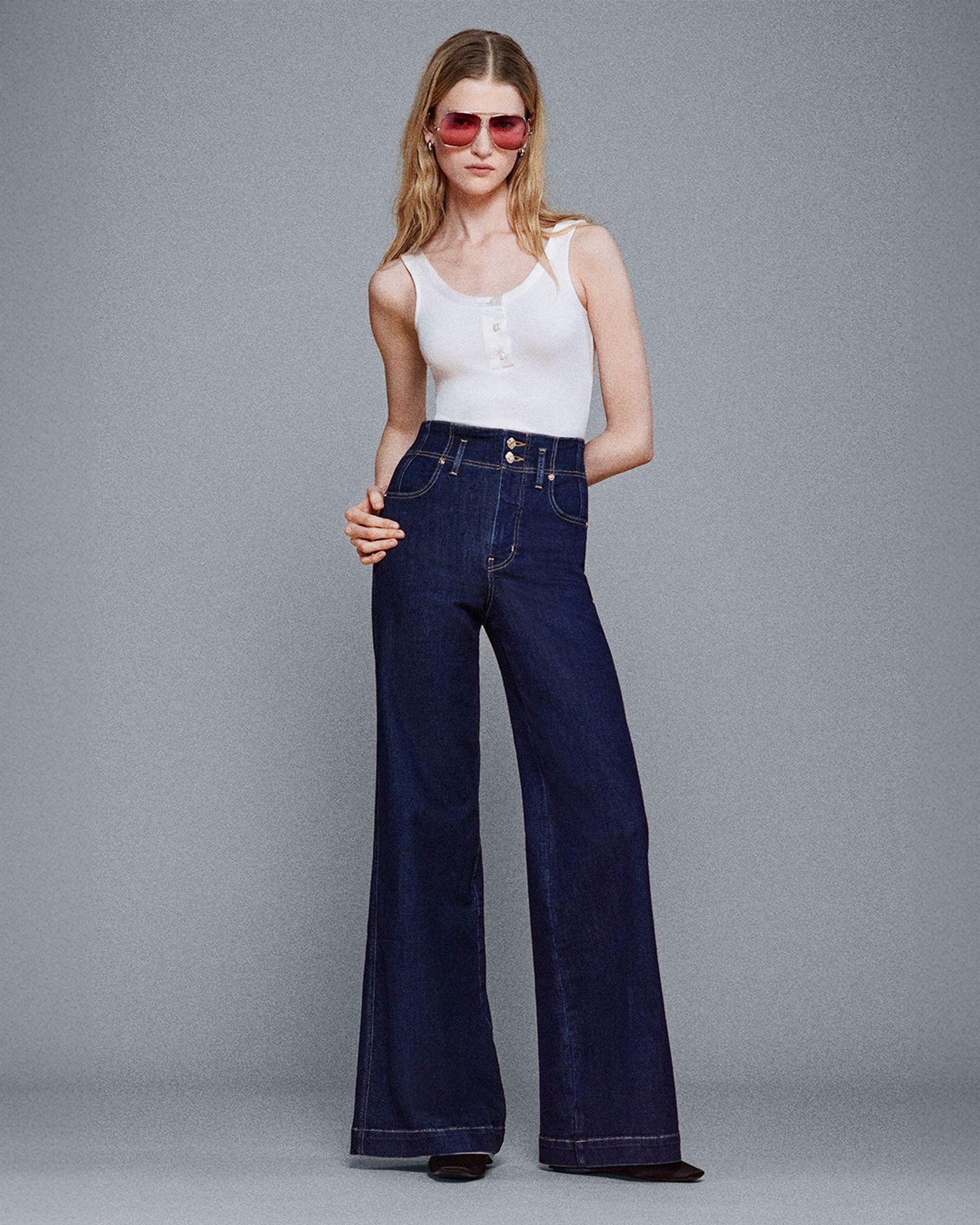 1 photo of female model in white tank and Frame bell bottom jeans, in blue denim.