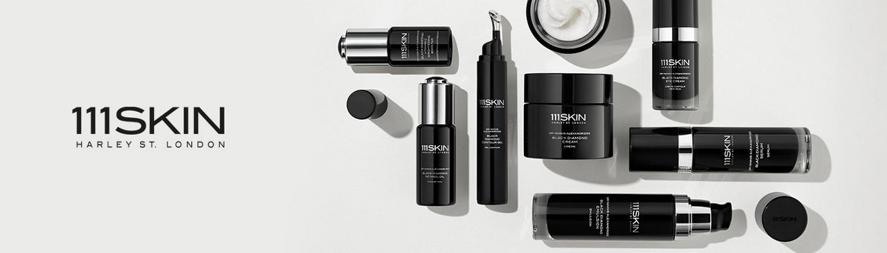 1 photo, an overhead shot of a variety of 111 skin black bottles and tubes of skincare, some with the caps off, arranged in a rectangular pattern.