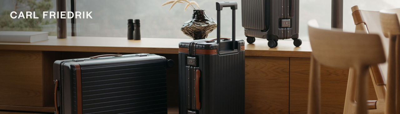 1 photo, of black and dark brown Carl Friedrik luggage next to a wooden sideboard in front of a glass window.