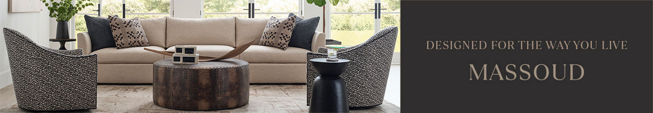 1 photo, of a living room setting with a long cream Massoud sofa flanked by 2  black and cream patterned swivel chairs, a round brown coffee table, and a small circular side table, floor to ceiling windows in the background.