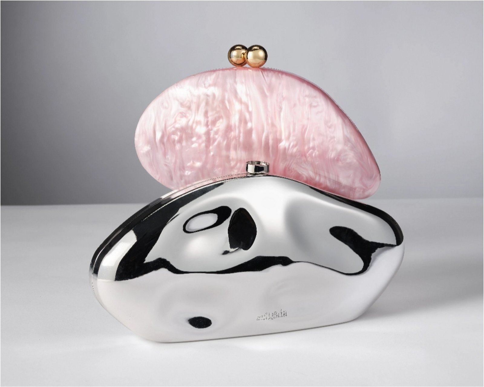 A pink pearl metallic clutch behind a sculptural silver metallic clutch.