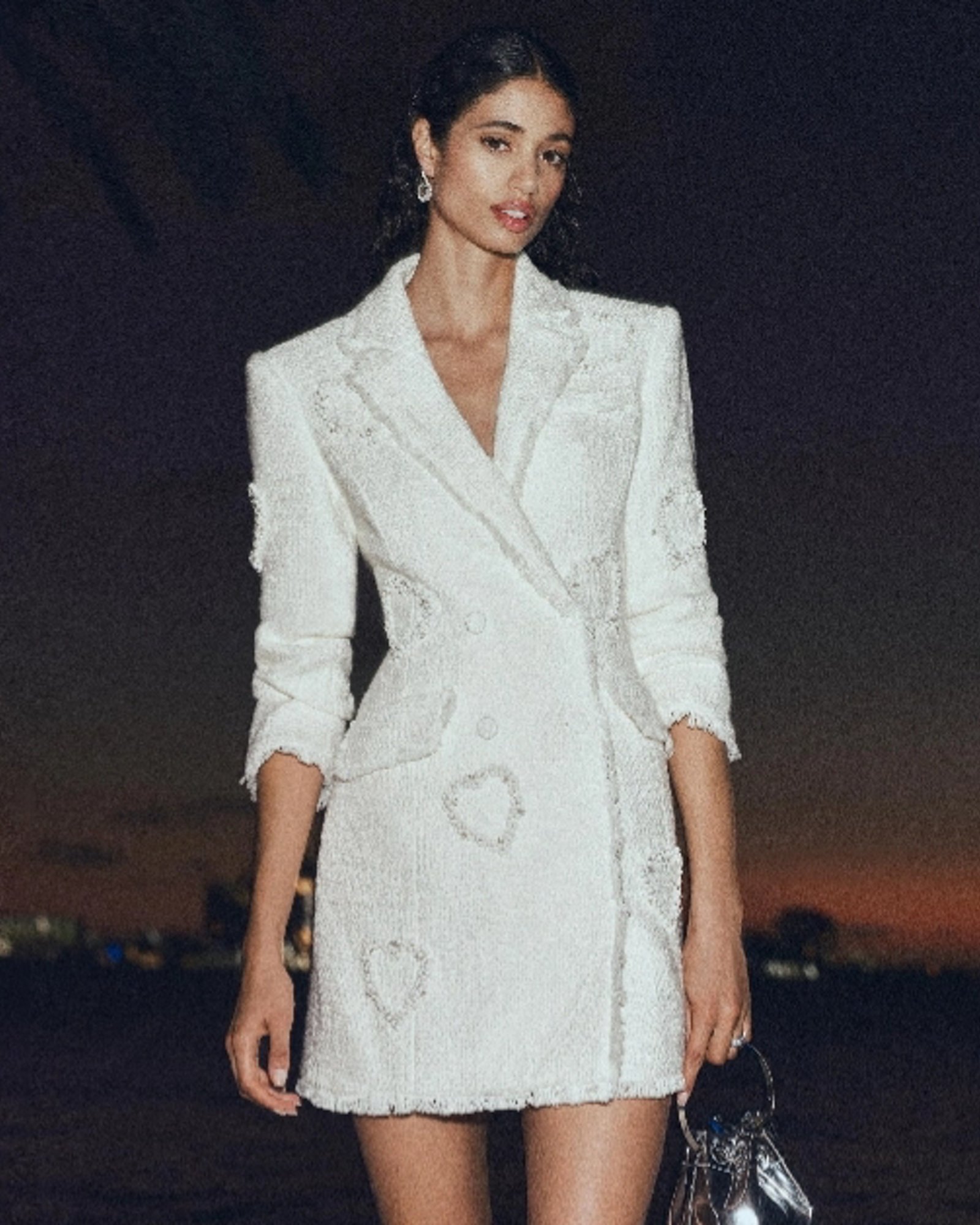 A woman in a long sleeve white blazer dress with heart silhouettes embroidered on it.