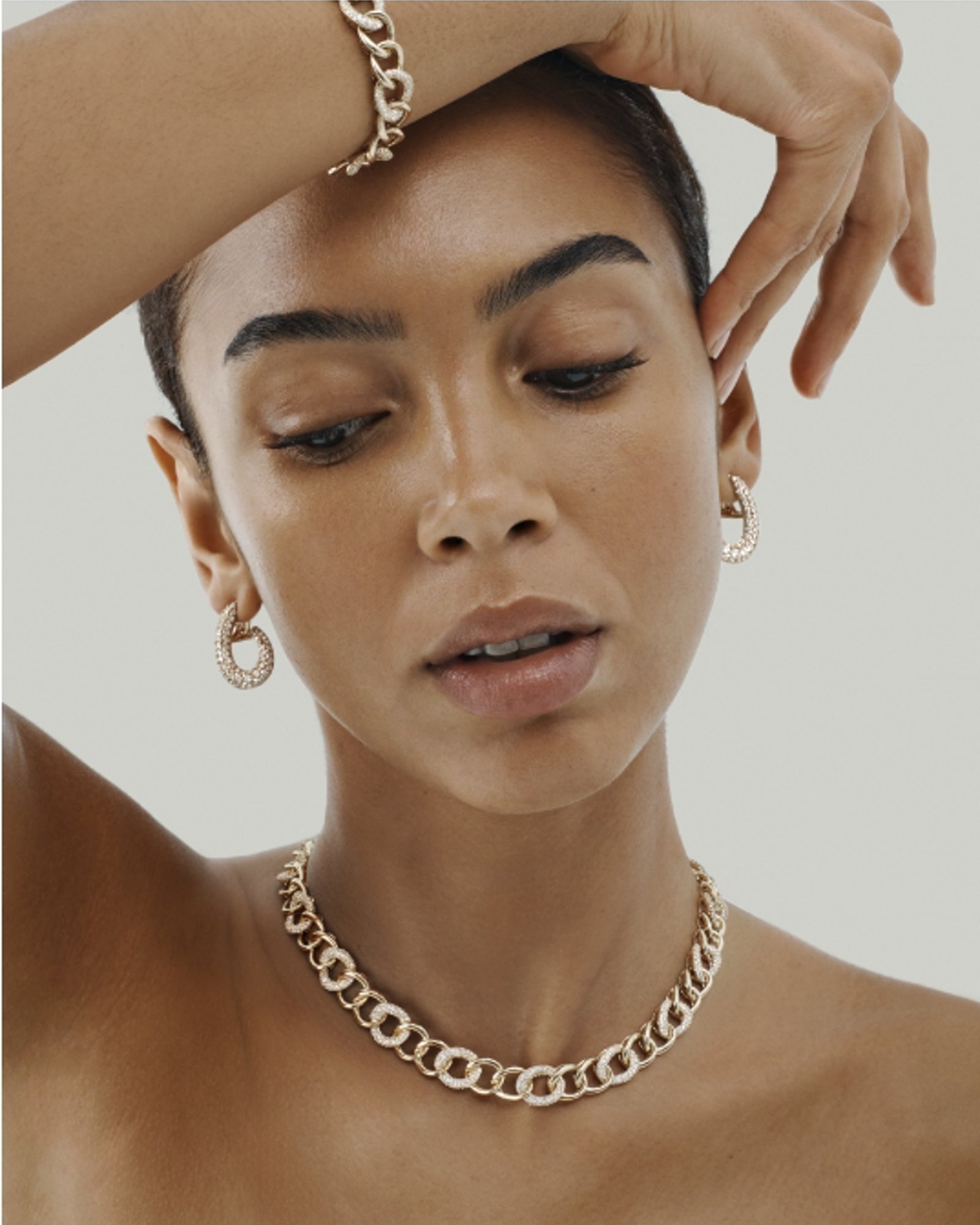 A woman wearing a yellow gold and diamond link choker and matching bracelet and earrings.