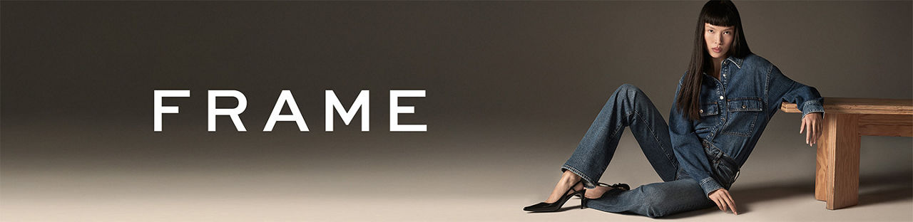 Frame. A woman sitting on the ground in a blue denim Frame shirt and jeans.