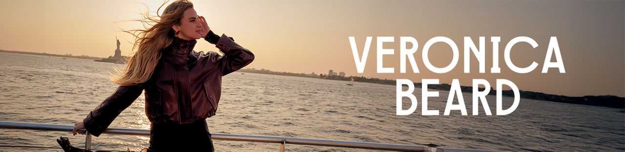 Veronica Beard. A woman in a brown leather jacket, standing in a boat with the Hudson River and the Statue of Liberty in the background.
