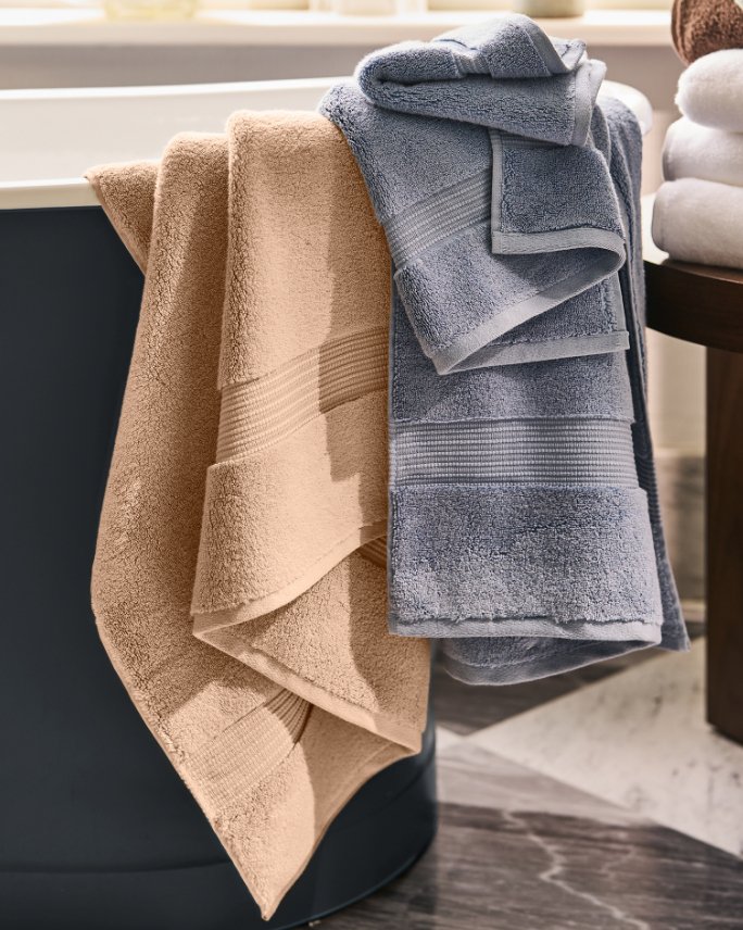 A tan and gray blue towel hanging over the edge of a tub.
