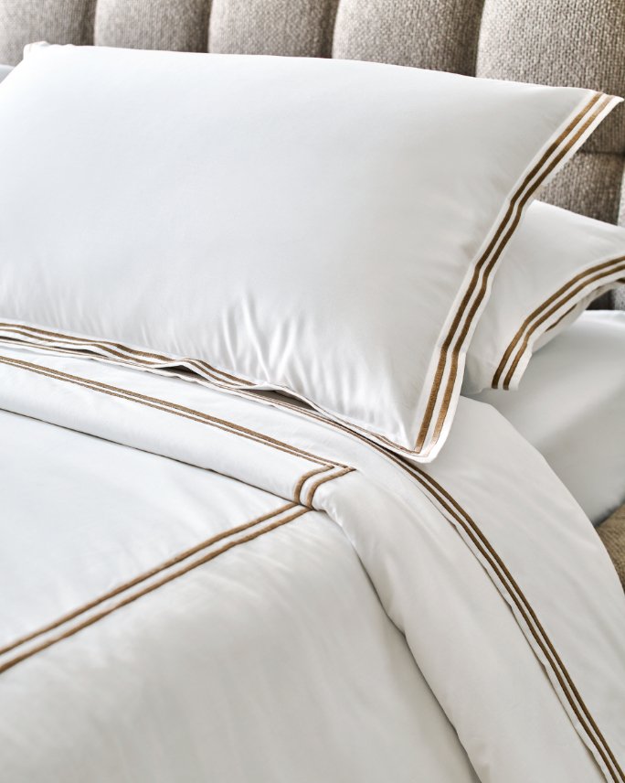 A bed made up with white with brown stitching linens.