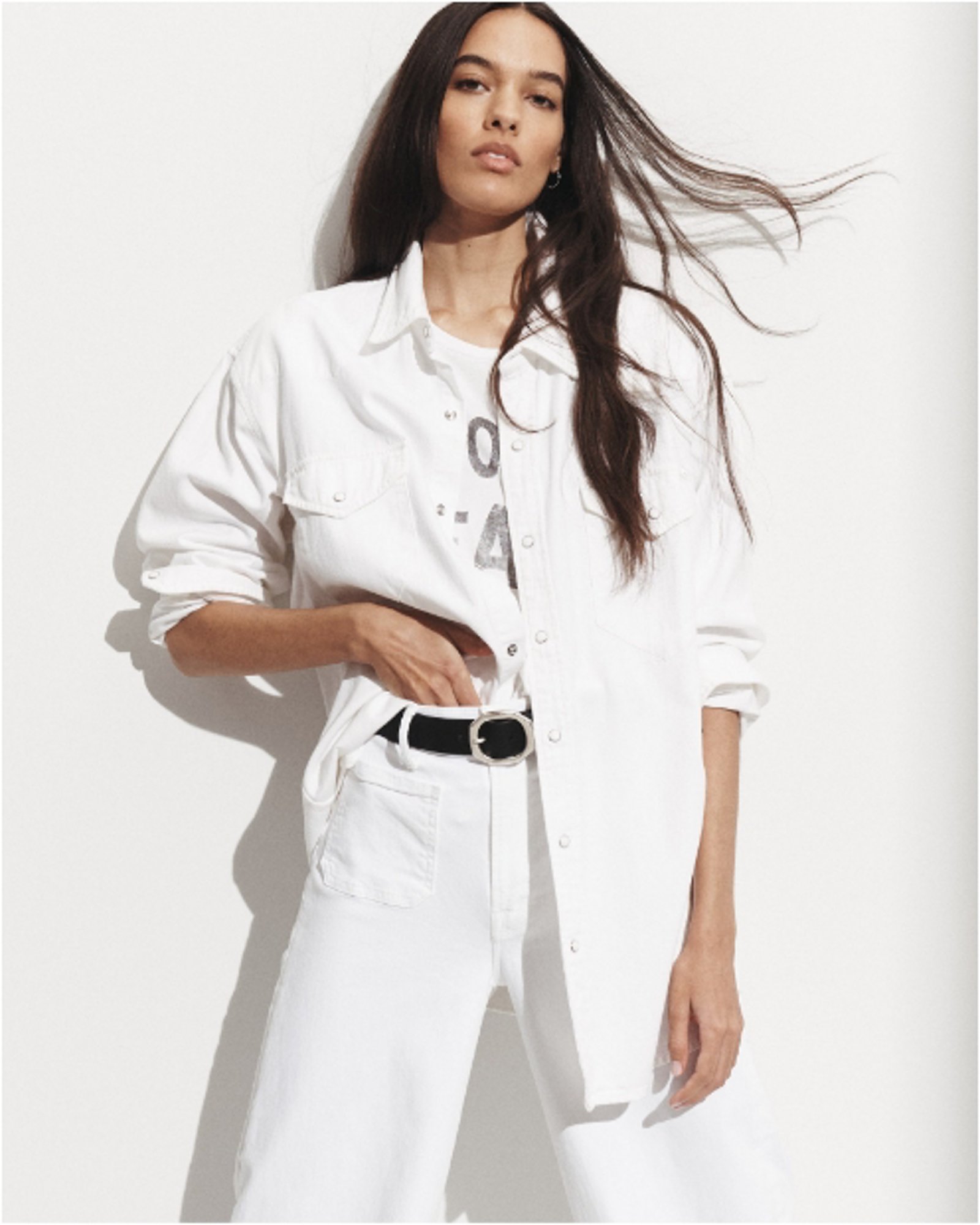 A woman in an open white button down over a white tee and white jeans.