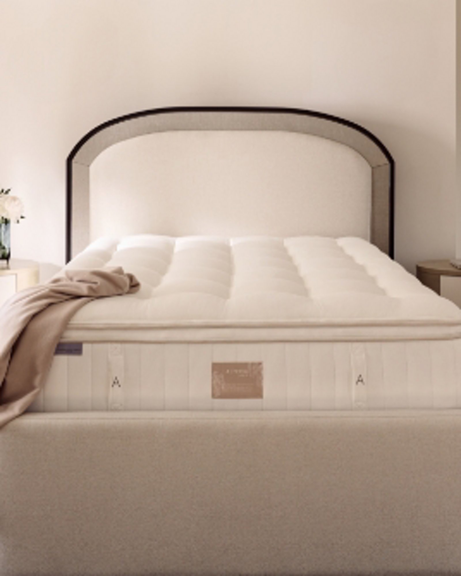 Closeup of white mattress with khaki throw draped at the corner, with a white and gray headboard, in a cool lit room.