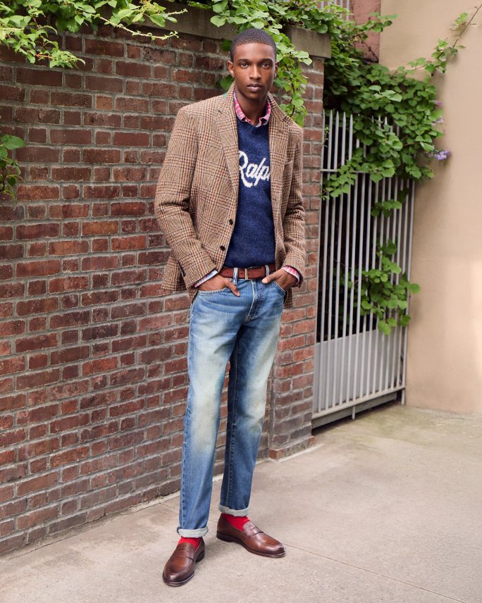 1 male model in navy blue graphic tee shirt, brown blazer, blue jeans, and brown leather loafers.