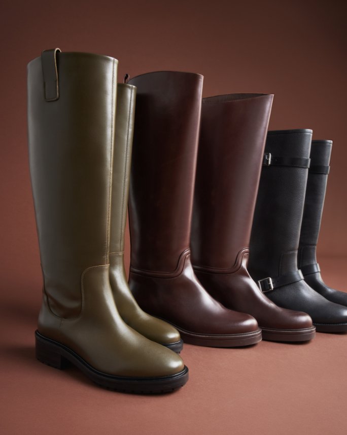 Three pairs of leather riding boots lined up next to one another, 1st in olive green, 2nd in dark brown, and 3rd in black.