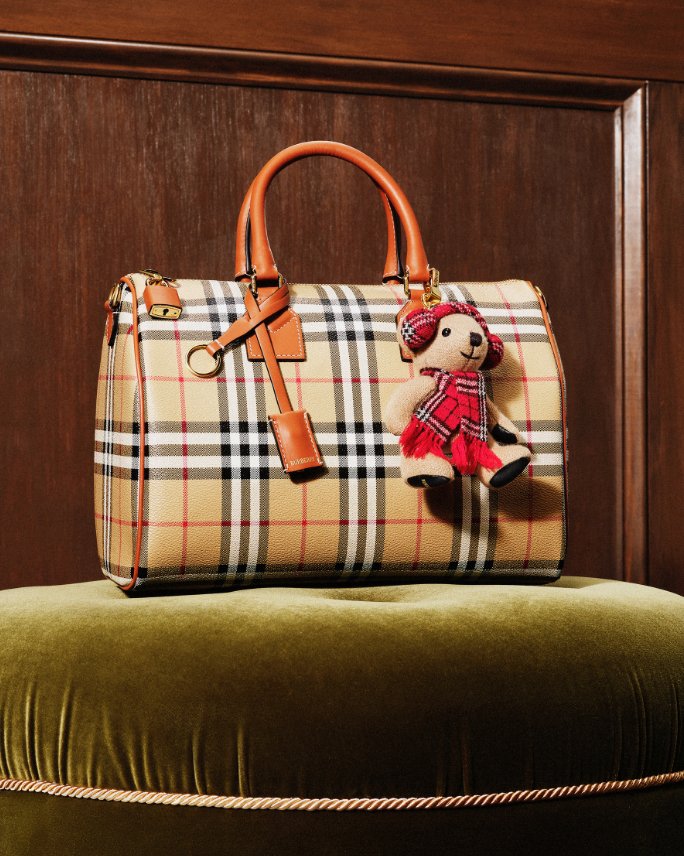 A Burberry plaid top handle bag with a Bloomingdales and Burberry teddy bear bag charm.