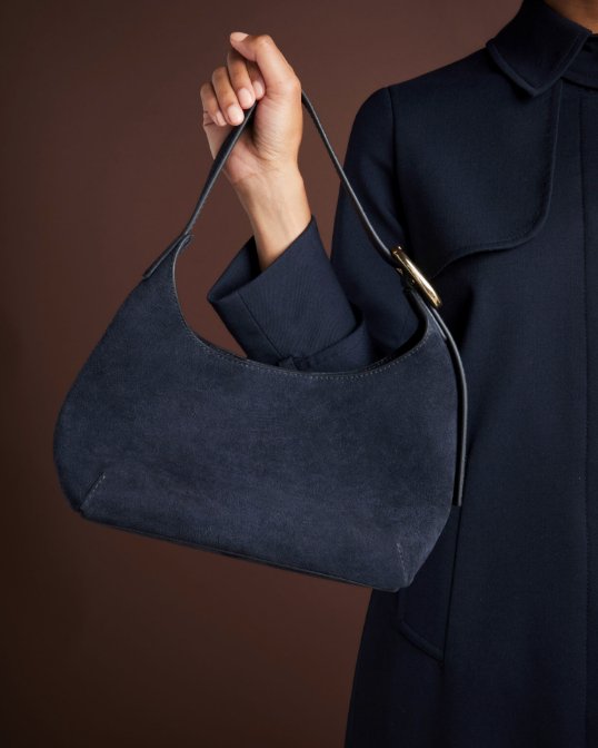A hand holding up a small blue suede bag.