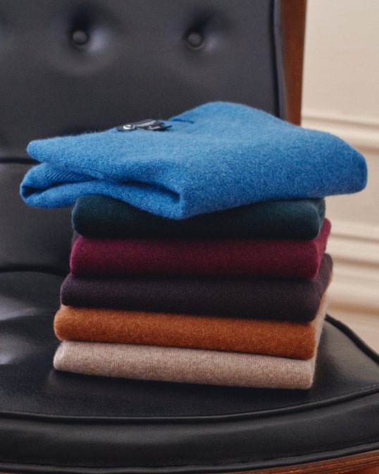 A stack of folded sweaters in different colors on a chair.