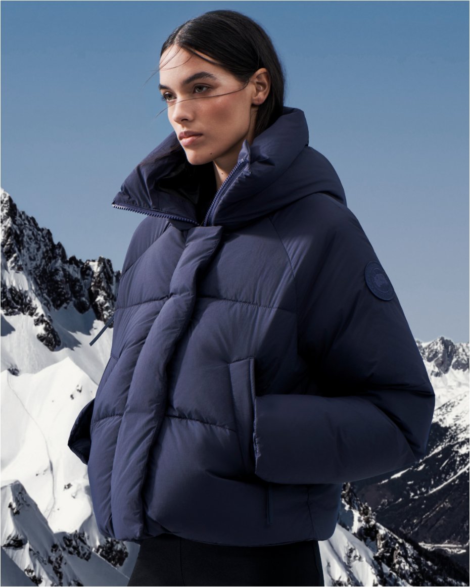 A woman on a snowy mountaintop in a dark blue Canada Goose puffer jacket.