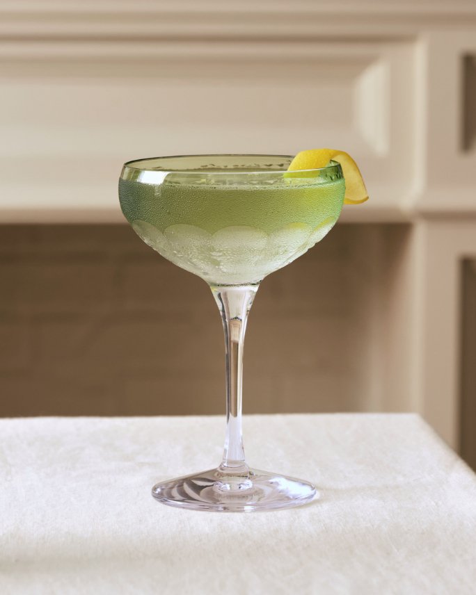 A martini glass filled with a light greenish liquid and lemon peel.