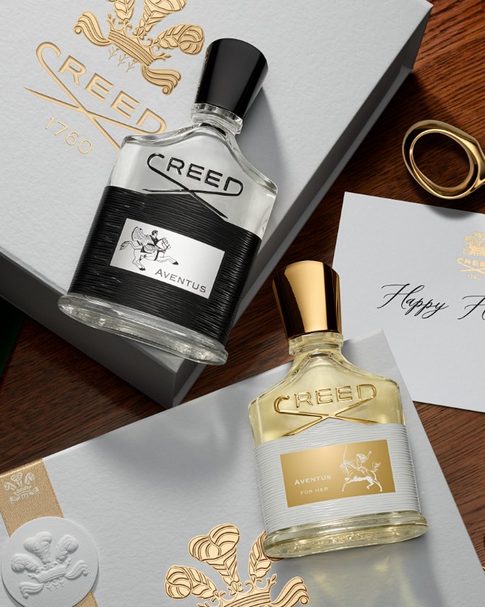 Bottles of Creed fragrances lying atop gold embossed Creed gift boxes.