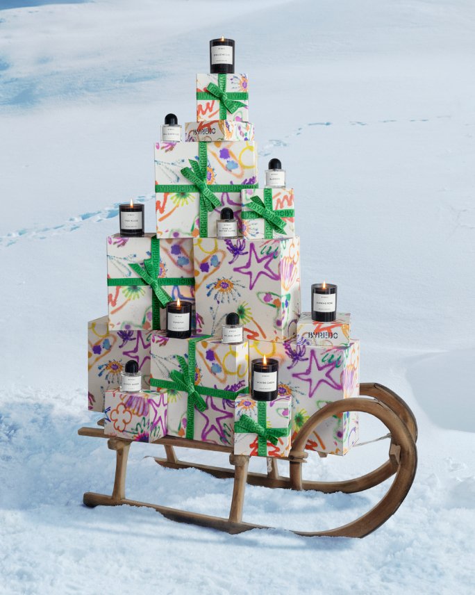 Festive Byredo boxes, perfume bottles and lit candles piled on a small sled.