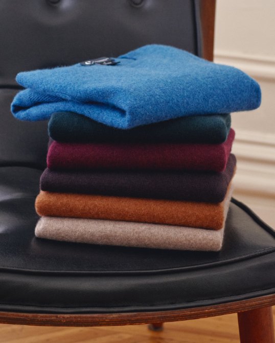 A folded pile of cashmere sweaters of different colors on a chair.
