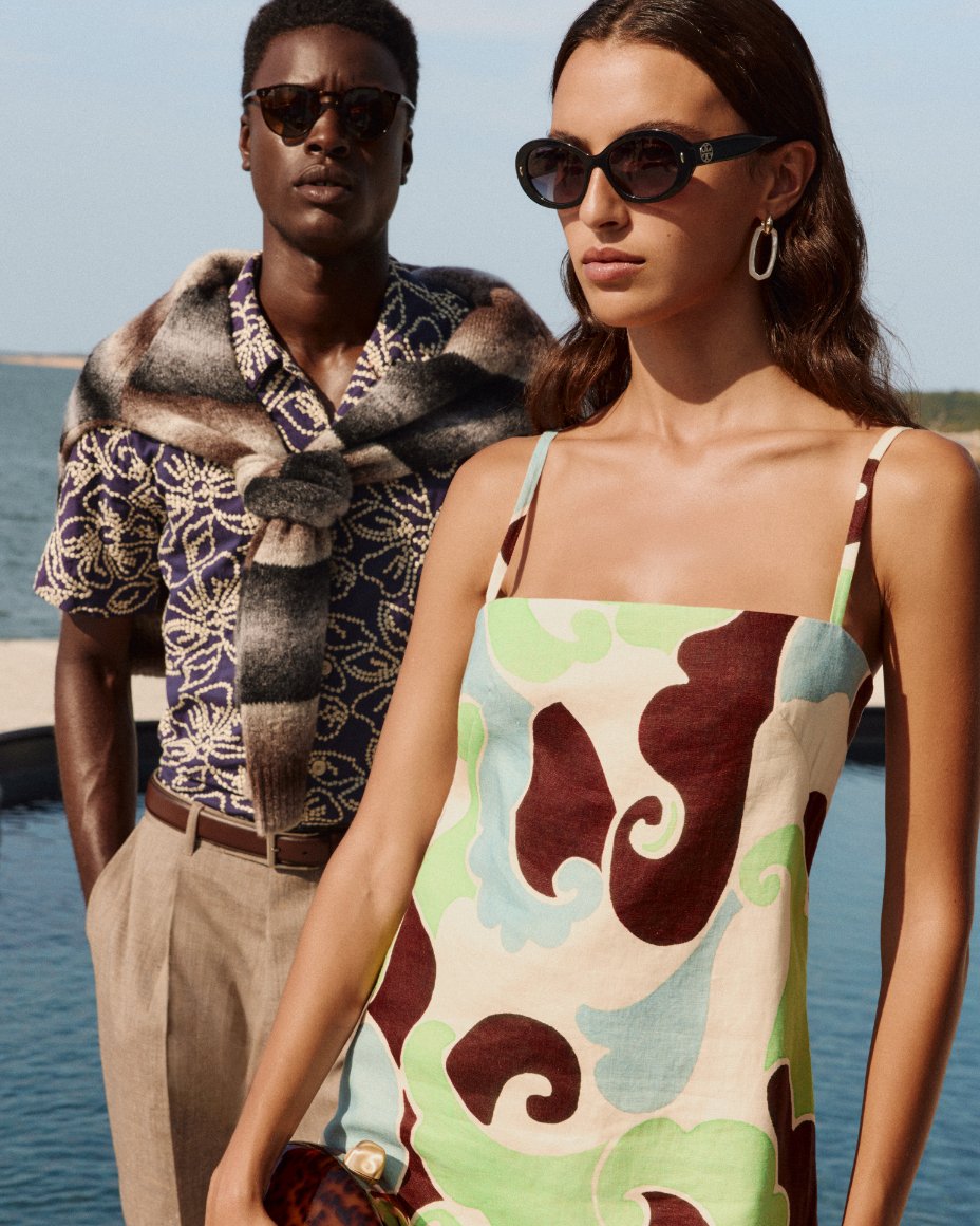 A man and woman standing near the water in resort wear clothing.