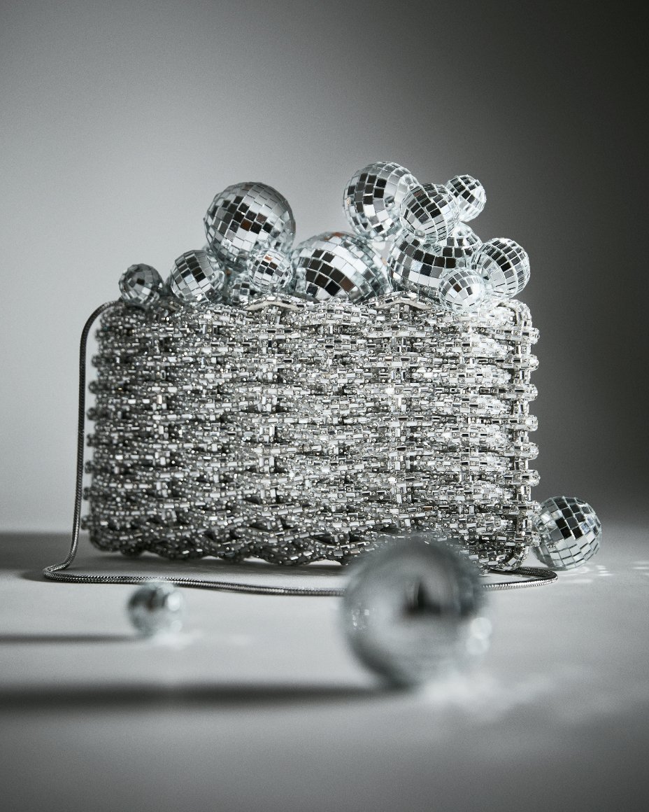 A silver metallic handbag surrounded by mini disco balls. Shop New Years Eve Dressing. 