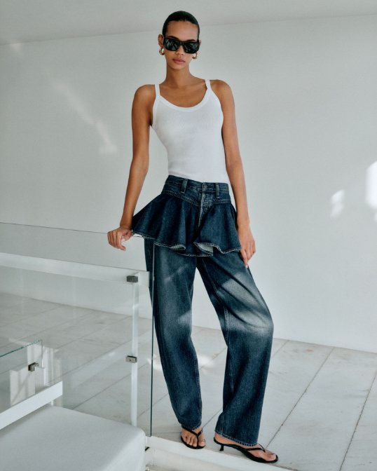 Female model with black sunglasses, wearing white thank top and blue denim skirt jean combo, with black sandals.