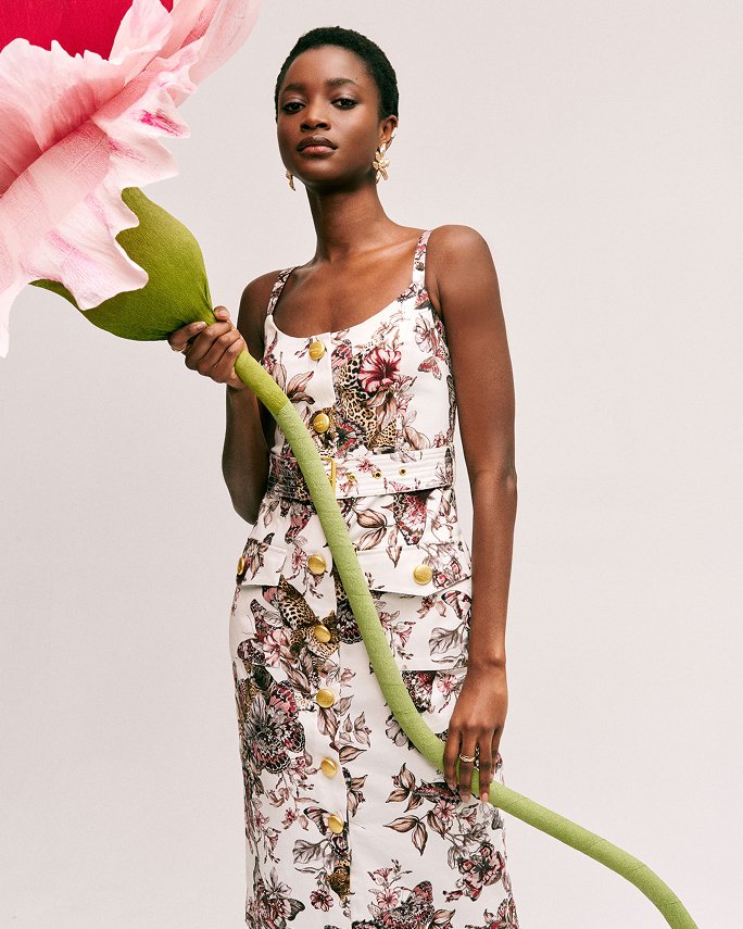 A woman in a sleeveless floral L Agence dress, holding a life size flower. Labels we love, L Agence.