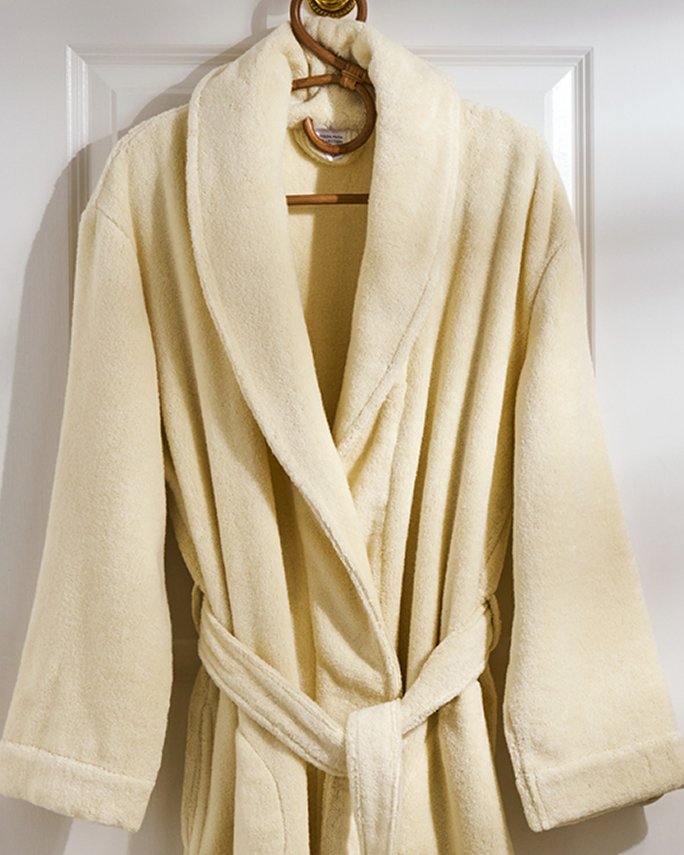 A butter yellow robe hanging on a hanger on the back of a bathroom door. Dorm room essentials, bath.