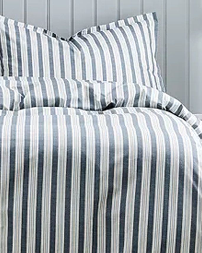 A bed made up with a light and dark blue striped comforter & pillow. Dorm room essentials, bedding & sheets.