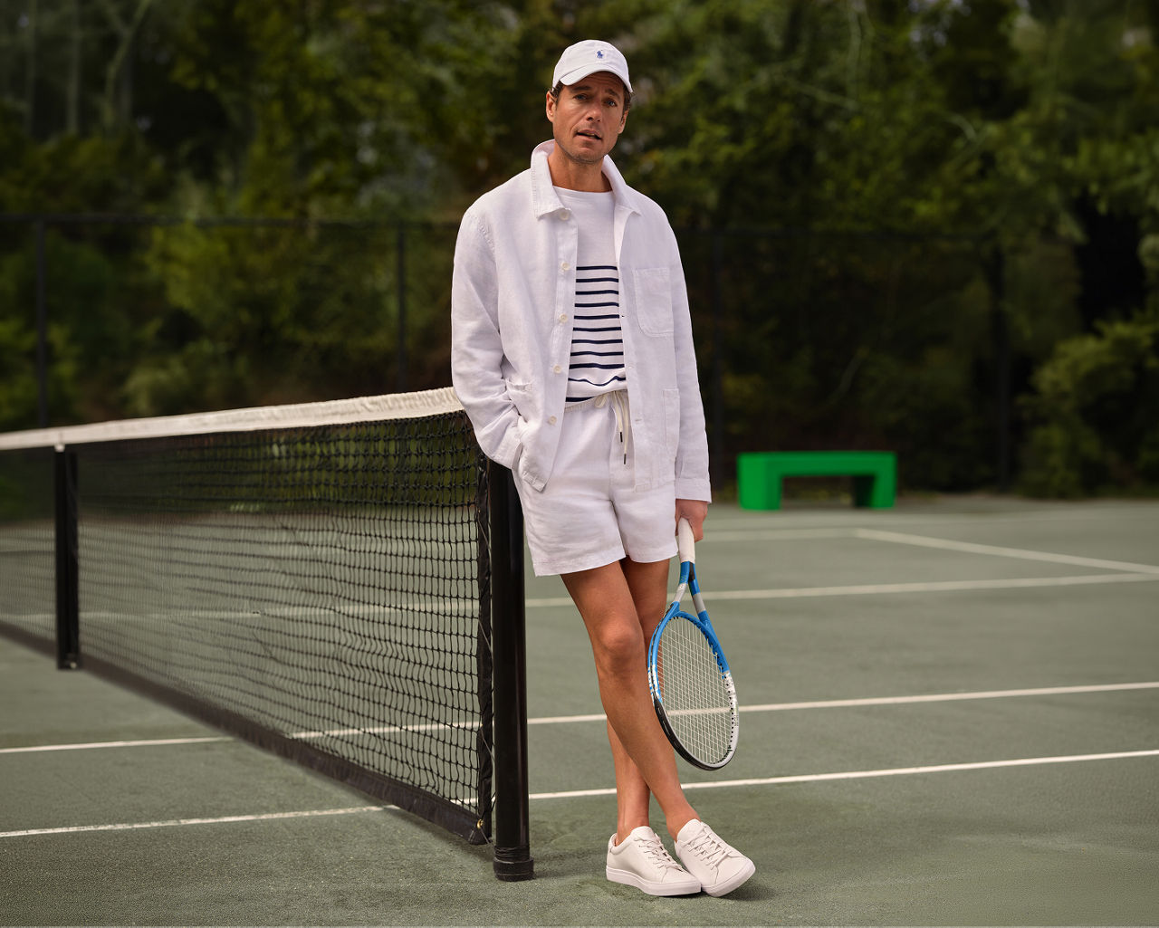 A man standing on a tennis court in an all white tennis outfit.