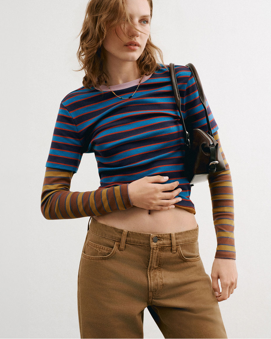 A woman in a striped shirt & low rise brown jeans. Shop low rise jeans.