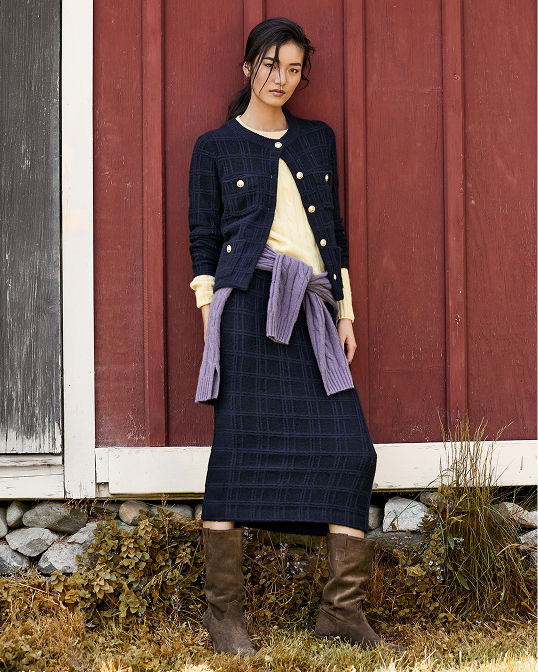 A woman in a dark blue argyle cardigan and matching midi skirt. Shop sweaters & knits.