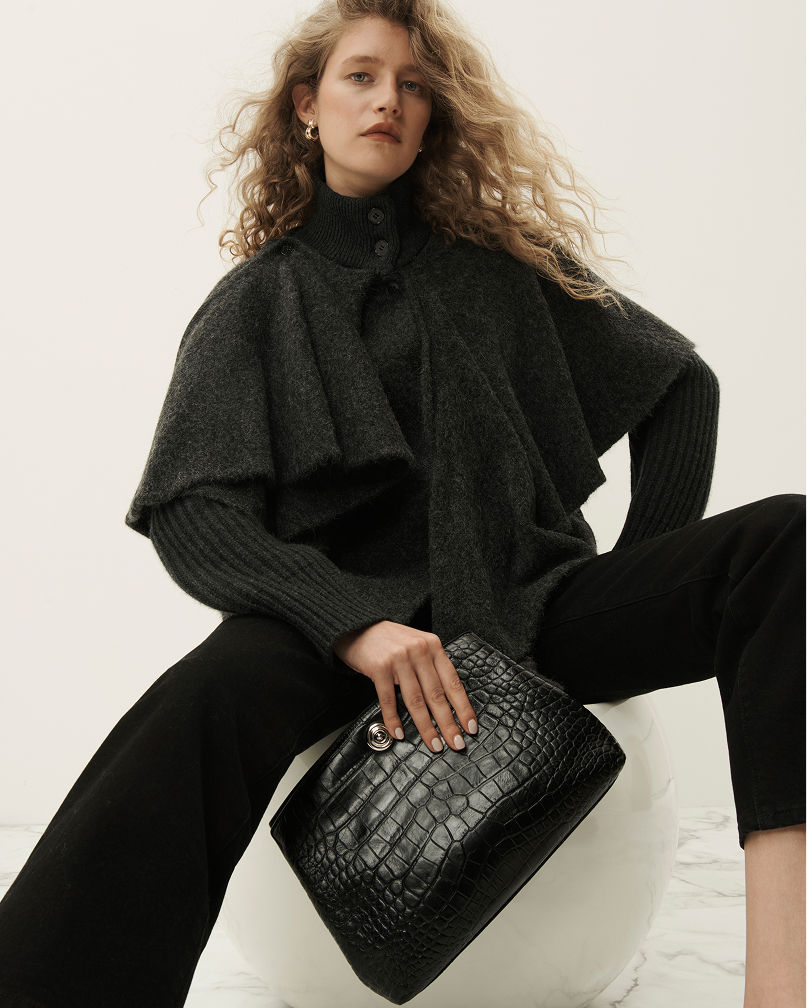 A woman in a gray structural outfit with a large black crocodile print clutch. Shop  modern clutches.